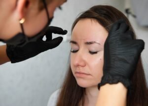 Browist makes eyebrow correction with tweezers thread. A model with dark hair in a light studio